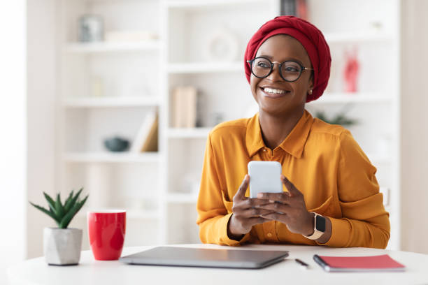 dreamy stylish black woman using mobile phone and smiling - minority professional occupation business ethnic imagens e fotografias de stock