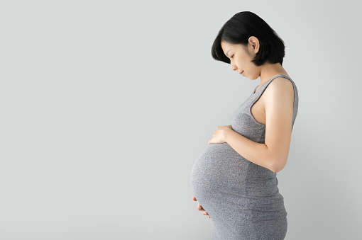 Pregnant Asian woman standing and touching big belly with her hands on gray Isolated background, Beautiful woman holding her stomach