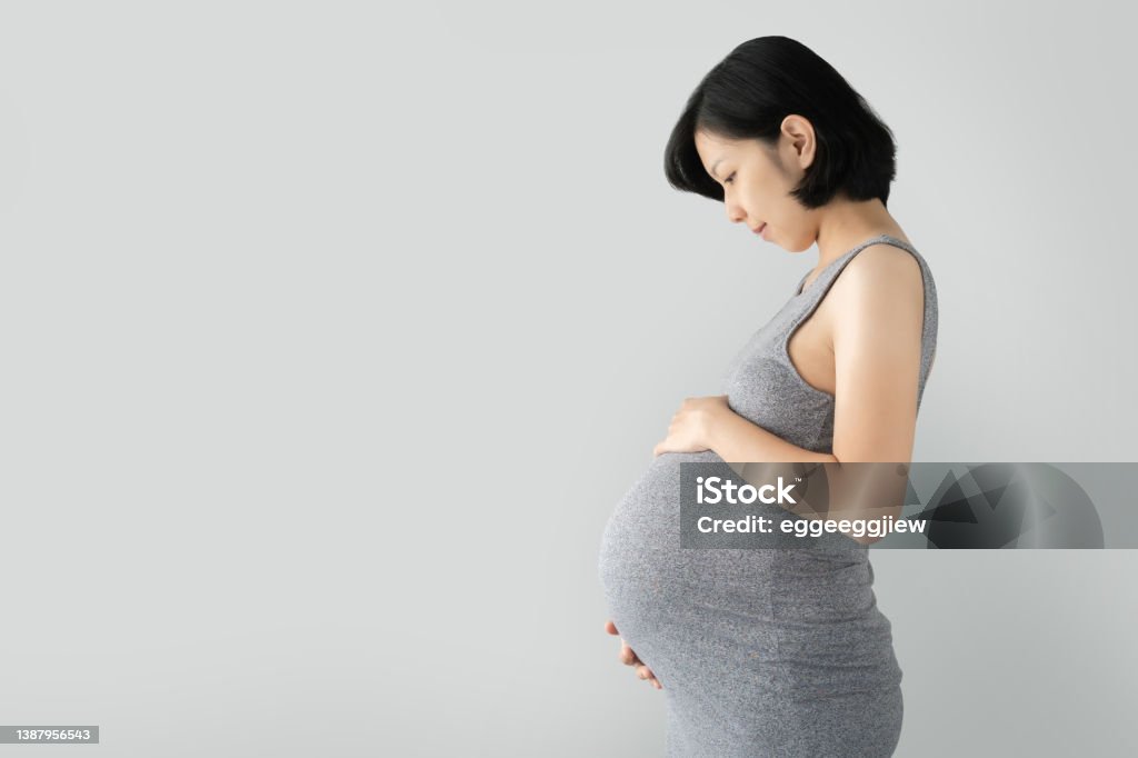 Pregnant Asian woman standing and touching big belly with her hands Pregnant Asian woman standing and touching big belly with her hands on gray Isolated background, Beautiful woman holding her stomach Pregnant Stock Photo