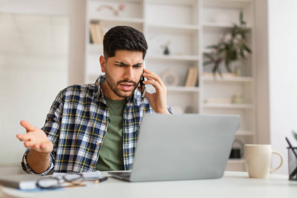 istock Angry Arab man talking on cell phone using laptop 1387958212