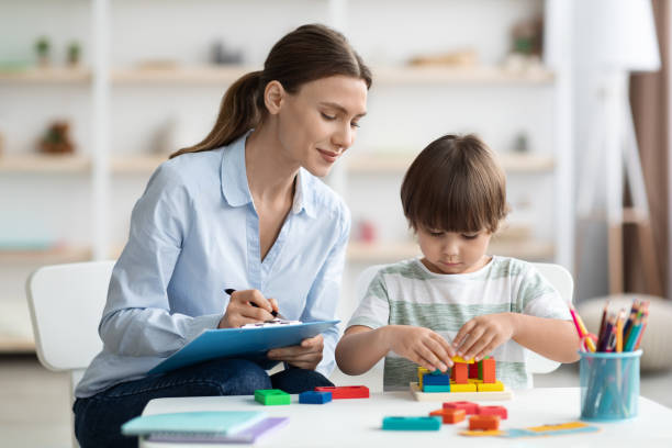 Assessment of kids mental development. Professional woman psychologist watching little boy playing with logical game Assessment of kids mental development. Professional woman psychologist watching little boy playing with logical game, evaluating his readiness for preschool, free space alternative therapy stock pictures, royalty-free photos & images