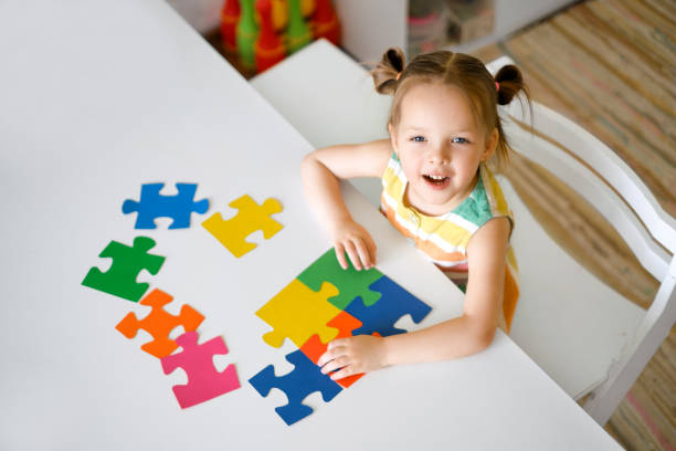istock Girl is sitting at a table and assembling a puzzle of elements on autism Day. 1387961616