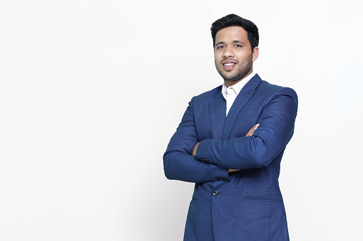 Portrait of a confident young indian man wearing suit standing with his arms cross, isolated on white studio background.