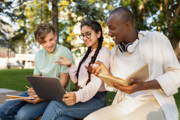 istock Happy diverse students studying together in park, preparing for test and looking at laptop screen, sitting in park 1387963872