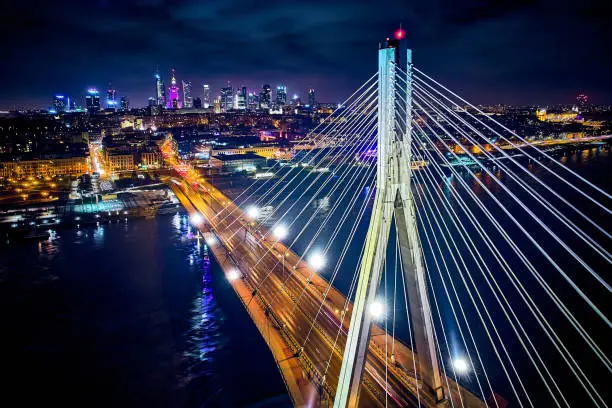 Beautiful panoramic aerial drone skyline view of the center of night Warsaw with skyscrapers in the background with the Swietokrzyski suspension bridge - the lights of the big city by night, Poland.