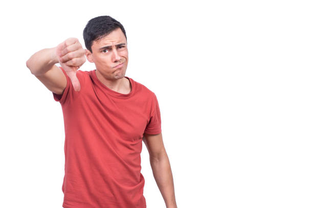 Sceptic guy giving thumb down gesture in studio Brunet in casual clothes looking at camera while standing on white background with thumb down thumb down stock pictures, royalty-free photos & images