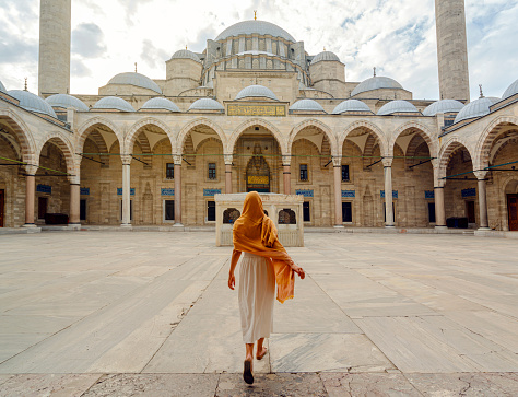 Istanbul, Turkey - 14 September, 2021: Female tourist with headscarf walking into Suleymaniye Mosque at sunset. Rear view. Suleymaniye Mosque, is the second largest mosque in the city, and one of the best-known sights of Istanbul, Turkey
