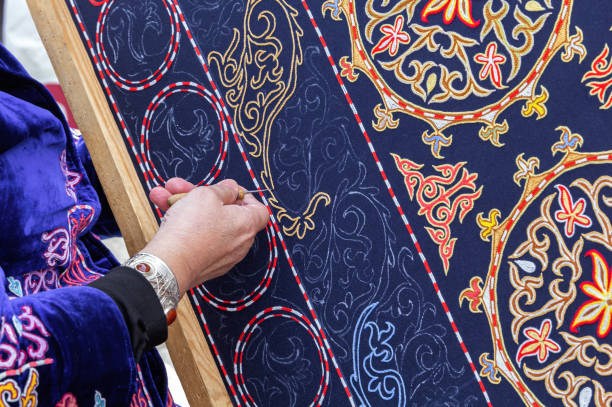 istock Woman's hand embroiders an Asian ornament on a carpet with gilded thread. Handmade 1387968002
