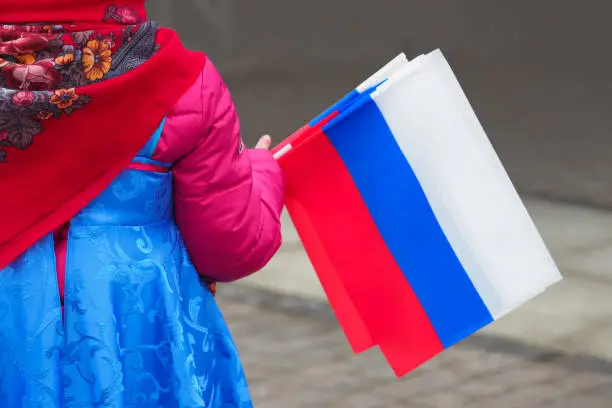 Little girl in national Russian clothes with Russian Federation flags in her hand, patriotism