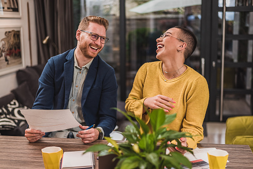 Delighted bearded man, telling a funny joke to his short haired, female coworker.