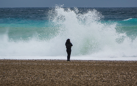Antalya, Turkey - November 27, 2021: Alone young woman standing in front of large waves on the Konyaalti Beach, Antalya