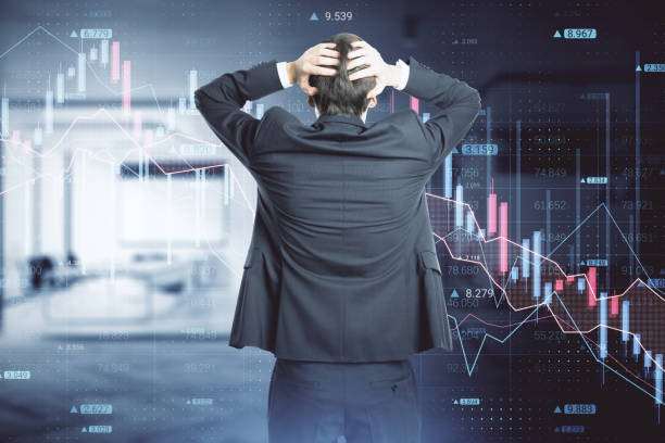 istock Back view of stressed out businessman looking at abstract downward forex chart on blurry office interior background. Crisis, finance and collapse concept. Double exposure. 1387976928
