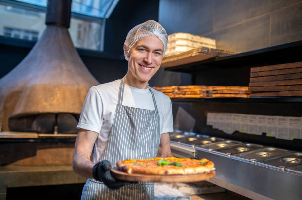 istock A chef in apron and hair cap preparing pizza 1387978470