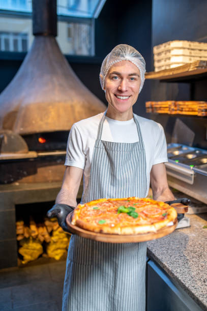 istock A chef in apron and hair cap preparing pizza 1387978478