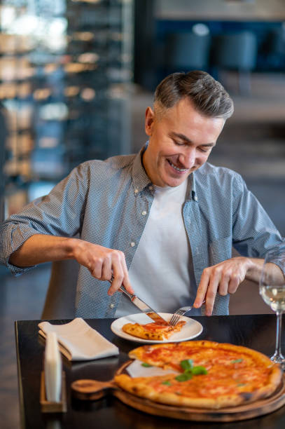 istock A smiling man sitting at the table and eating pizza 1387978532
