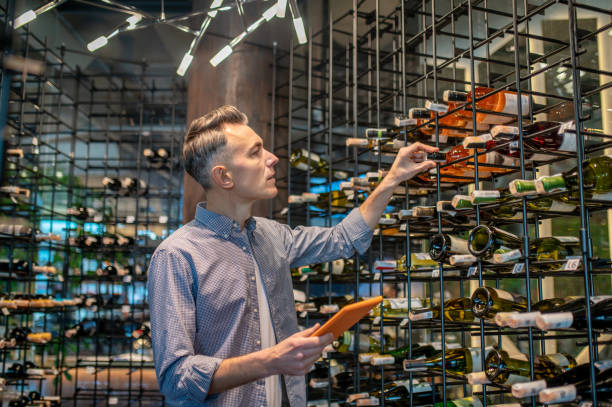 mężczyzna w sklepie z winami z mnóstwem butelek z winem - wine bottle liquor store wine variation zdjęcia i obrazy z banku zdjęć