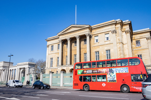 People and a double-decker bus in front of Apsley House on Hyde Park Corner at Piccadilly in City of Westminster, London. This was the residence of the first Duke of Wellington and his descendants. It was opened in 1778 after having been designed by Benjamin Dean Wyatt and Robert Adam in the neoclassical and Gothic revival style.