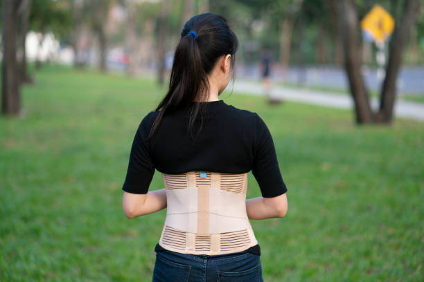 giovane donna asiatica che indossa supporto alla schiena per proteggere la schiena, la medicina e il concetto sano - busto ortopedico foto e immagini stock