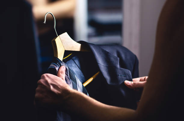 Man getting ready and dressing up in a suit. Luxury jacket and tie in hanger. Trying on outfit before date or wedding. Fitting room in mall store, closet or tailor shop. stock photo