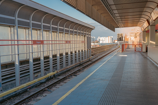 Surface metro station, stretching into distance, in rays of setting sun. Deserted platform, waiting for train. Vienna, Austria 03 2022