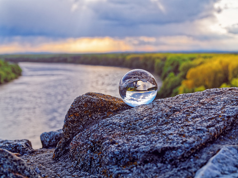 The magic glass ball is on old stones against the backdrop of sunset, river and forest. The concept of magic, mysticism, predictions, divination.