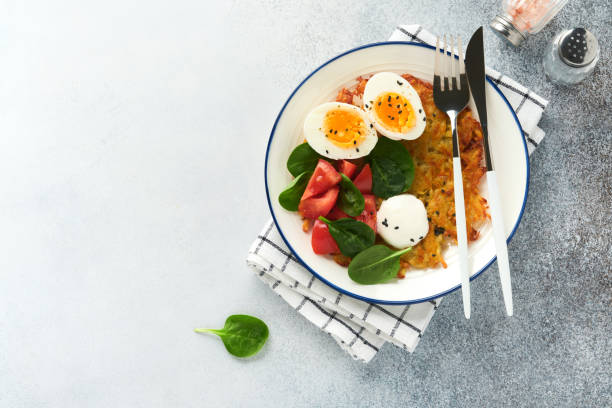 istock Breakfast. Potatoes latkes with sour cream, spinach salad, tomatoes and boiled eggs on light background.  Delicious food for breakfast. Top view. 1387999569