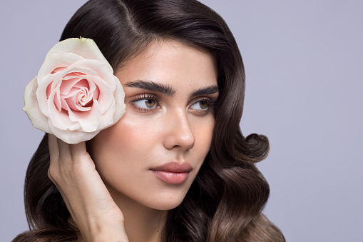 Close up studio shot of a beautiful brunette  woman with soft skin holding rose flower.