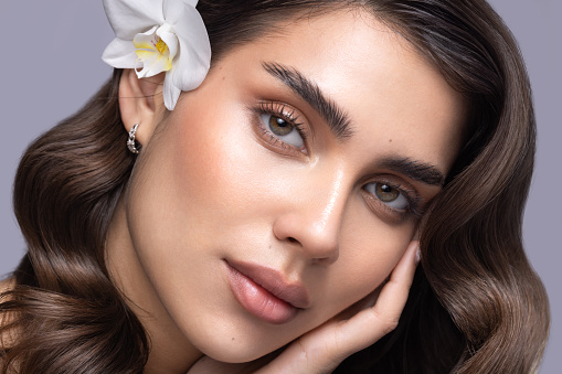 Close up studio shot of a beautiful brunette  woman with soft skin holding orchid flower.