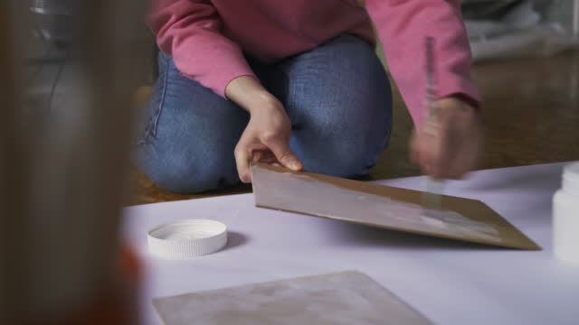 Woman artist dips a brush into a jar of white paint for drawing