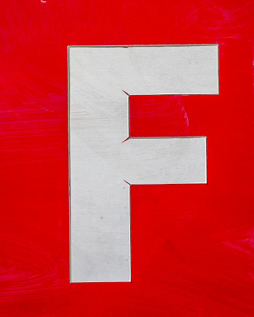 Close up of a dirty white letter F against a red background.