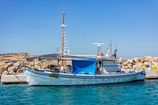 Greece. Wooden fishing boat moored at rocky construction port dock, Koufonisi Greek island, Cyclades. Aegean calm sea, blue sky
