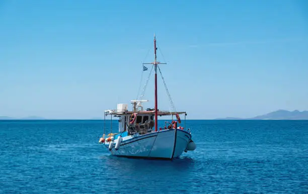 Wooden fishing boat moored in infinite Aegean calm sea, clear blue sky background. Koufonisi Greek island, Cyclades. Destination Greece, summer day.