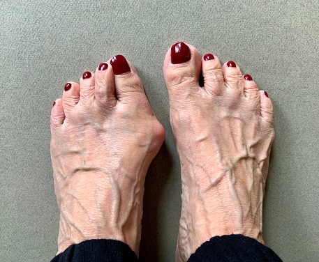 Women's pedicure with a  bright red gel polish and white inscription. Woman's legs with a maroon coating on the nails and white text design.