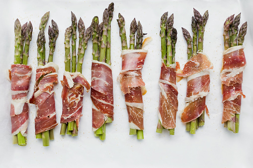 Asparagus with ham on white background. Tasty spring dish with asparagus and bacon