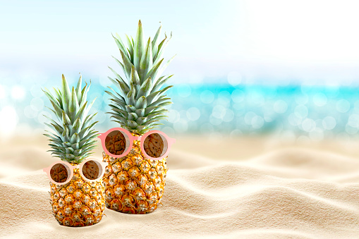 Pineapples in sunglasses on the beach. Tourism. White sand on the seashore. Tropical summer vacation. Family vacation. Travel.