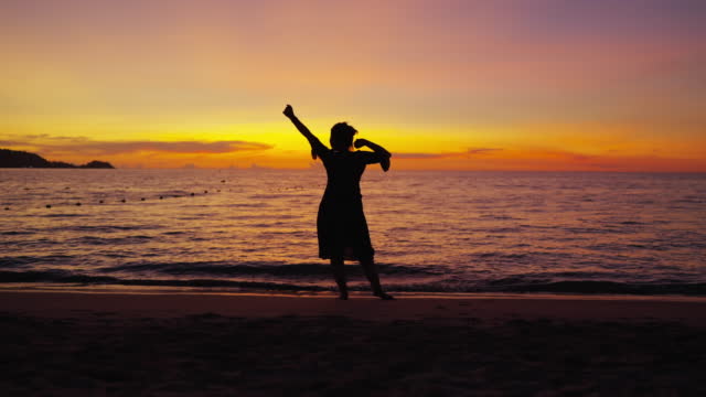 attractive asian female woman casual relax dance move with carefree freedom peaceful and enjoy wonderful moment ocean beach at sunset ,silhouette asian woman walk dance on the beach dramatic sky background