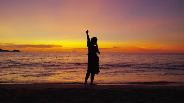 attractive asian female woman casual relax dance move with carefree freedom peaceful and enjoy wonderful moment ocean beach at sunset ,silhouette asian woman walk dance on the beach dramatic sky background