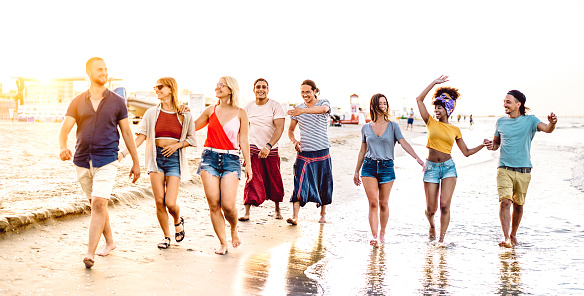 Large group of trendy happy friends walking at beach by sunset time - Multiracial life style concept with young people having fun on summer vacation - Bright vivid filter with focus on middle frame