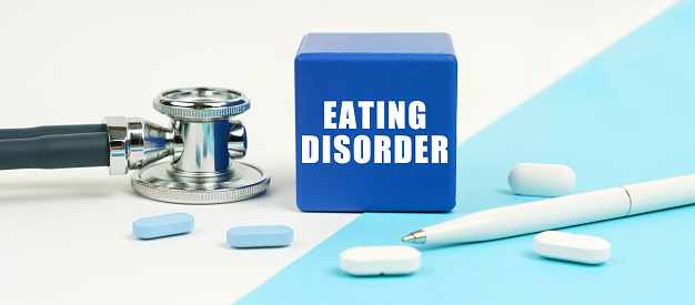 Medical concept. On a white and blue surface are pills, a stethoscope, a pen and a cube with the inscription - Eating disorder