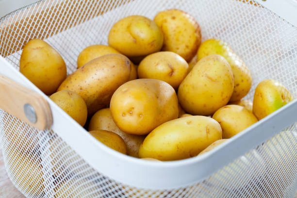 istock Raw potatoes in white wire basket on wooden background 1388024312
