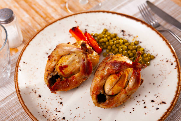 Two delicious oven baked quails served on plate with light vegetable side dish of carrot and green peas