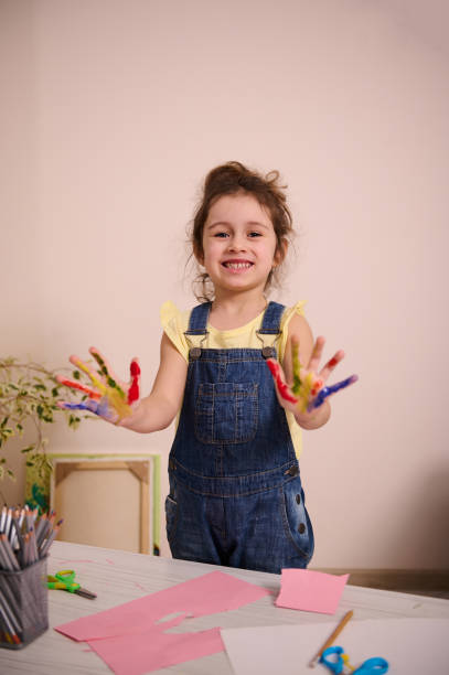 un bambino affascinante, una bambina carina di 4 anni sorride dolcemente mostrando le sue mani in vernice per la creatività alla macchina fotografica - 4 5 years foto e immagini stock