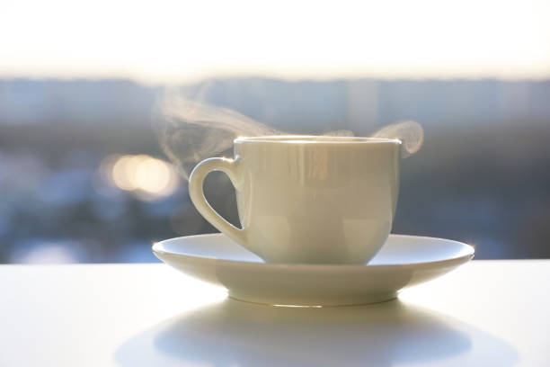 Hot coffee or tea cup with steam smoke on shining sun background stock photo