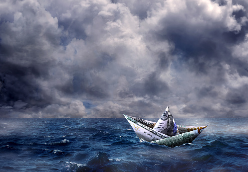 Conceptual dollar bill paper boat on dramatic seascape