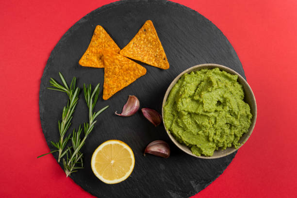 top view of homemade organic guacamole, garlic, lemon and tortilla chips on a slate plate on a red background. selective focus. - guacamole food bar vegan food imagens e fotografias de stock