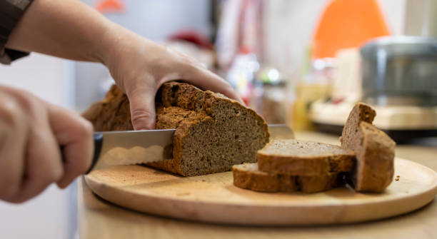 Freshly baked goodness Shot of an unrecognizable woman cutting a brown bread BROWN BREAD stock pictures, royalty-free photos & images