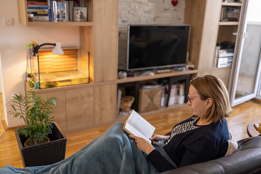 Portrait of a happy adult woman enjoying  reading a good book while sitting on her couch at home