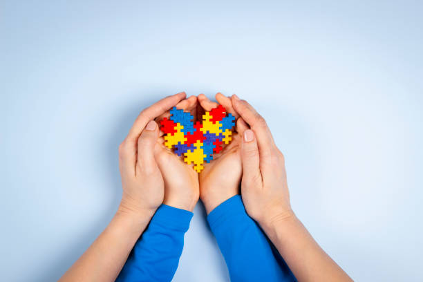 世界自閉症啓発デーのコンセプト。水色の背景にパズルハートを持つ大人と子供の手。トップビュー - 自閉症 ストックフォトと画像