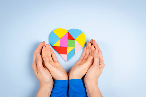 World autism awareness day concept. Woman and child hands holding puzzle heart on light blue background. Top view stock photo