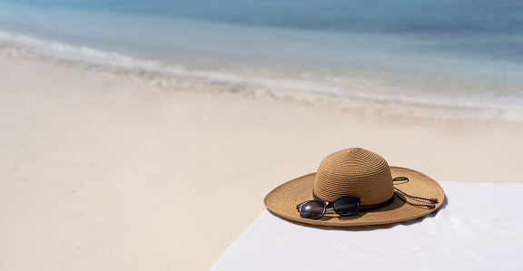 Straw hat on a sunbed on a background of white sand and sea of the Maldivian beach.